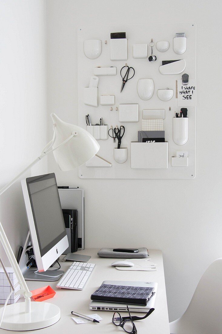 Weißer Schreibtisch mit Computerbildschirm und weißer Tischleuchte in Zimmerecke mit aufgehängtem Retro- Aufbewahrungsboard aus weißem Kunststoff