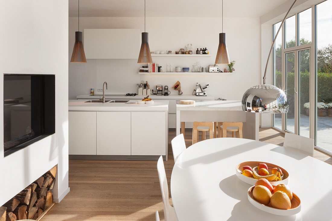 Ovaler, weisser Esstisch mit Obstschalen vor offener Küche und Fensterfront