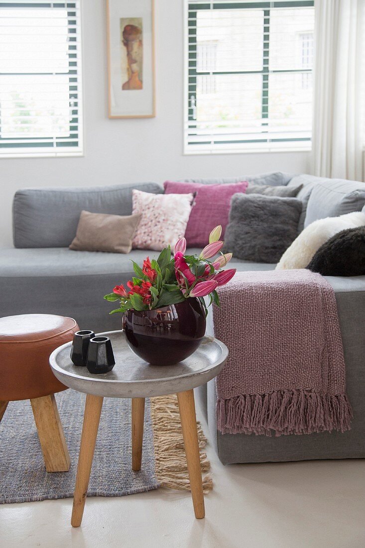 Dreibeintisch mit Blumenstrauß vor Sofa mit verschiedenen Kissen