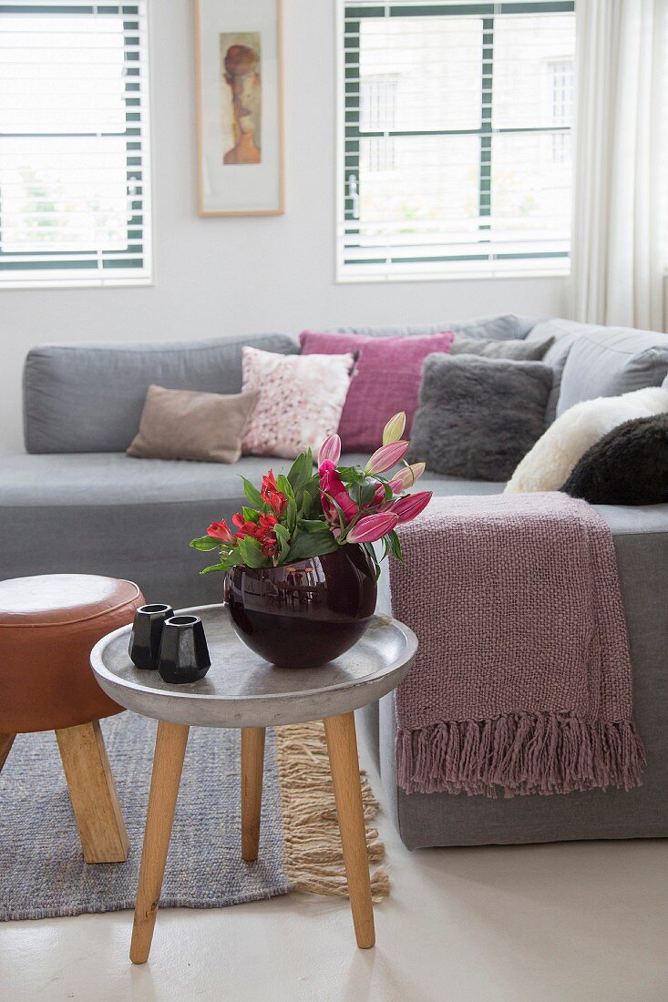 Vase of flowers on three-legged table in front of sofa with many scatter cushions