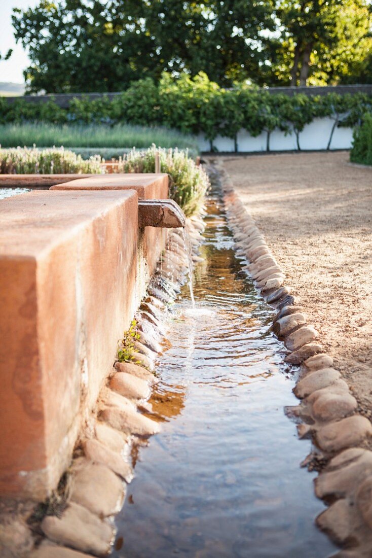 Plätschernder Brunnen mit langer Wasserrinne in sonnigem Hof