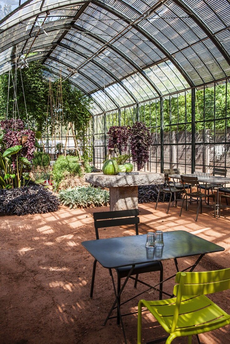 Luxuriant planting in greenhouse with central stone table and folding garden table