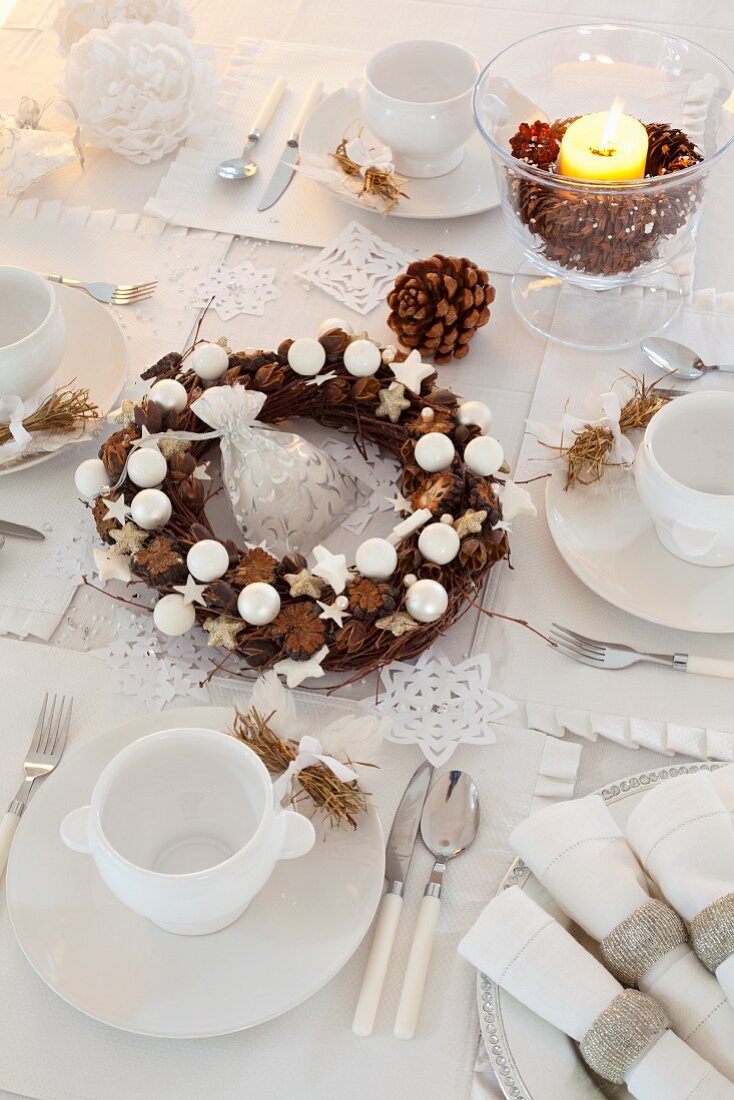 Weihnachtlich gedeckter Tisch in Weiß mit Tischkranz aus Zapfen & Kugeln
