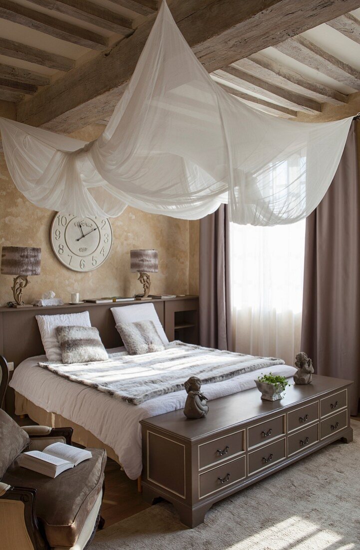 Elegantes Schlafzimmer mit aufgehängtem weißem Stoffsegel über Doppelbett an Holzbalkendecke