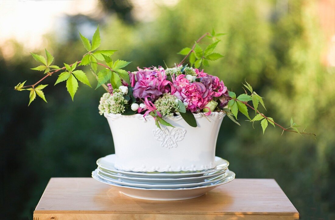 Sommerliches Blumenbouquet in weisser Porzellanschale auf Tisch im Freien