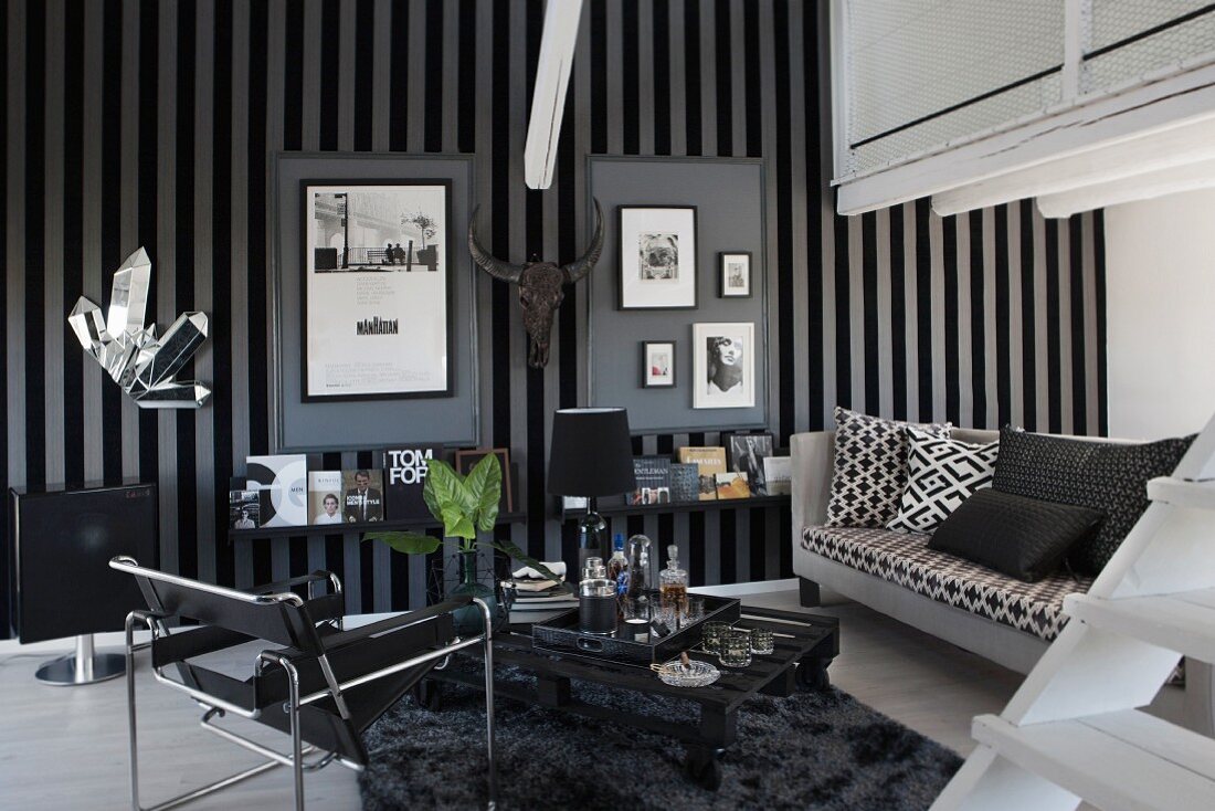 Maskuliner Wohnraum mit 'Wassily- Stuhl' und schwarz-weißem Sofa, im Hintergrund dekorierte Wand mit grau-schwarz gestreifter Tapete