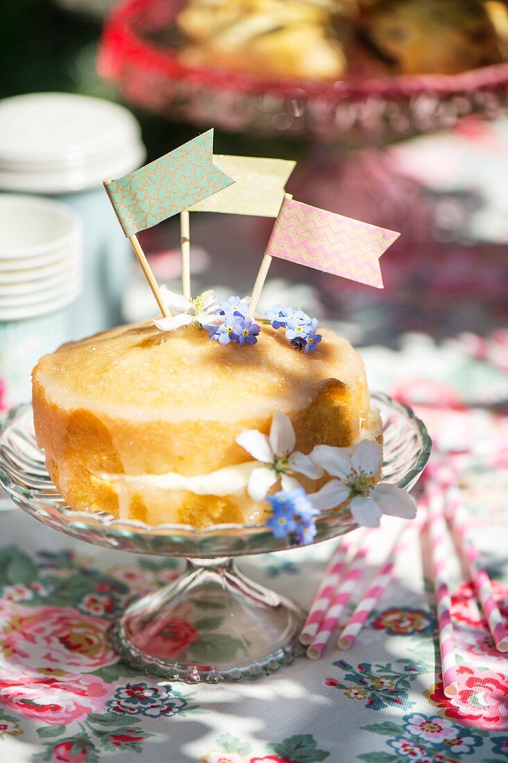 Kuchen mit Papierfähnchen und Essblüten dekoriert auf Kuchenständer