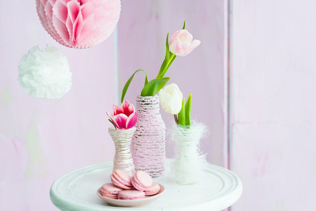Tulips in vases wrapped in cord next to plate of pink macarons