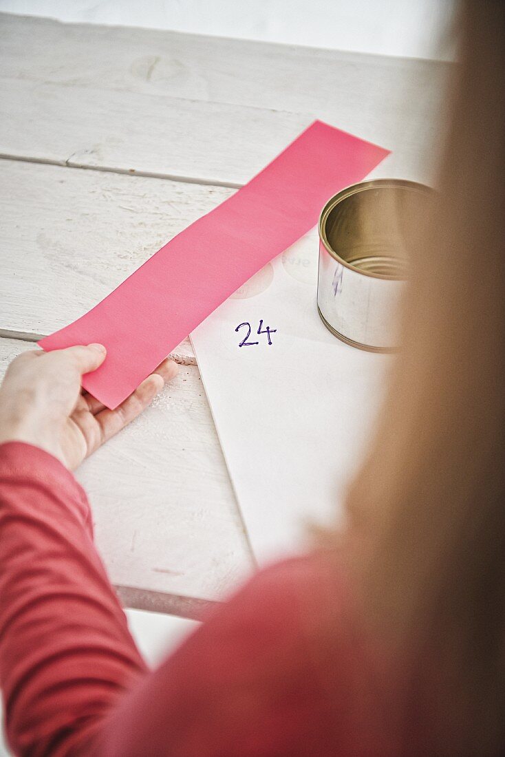 Blechdose, Aufkleber und rosafarbenes Papier in Mädchenhand für DIY-Adventskaldender