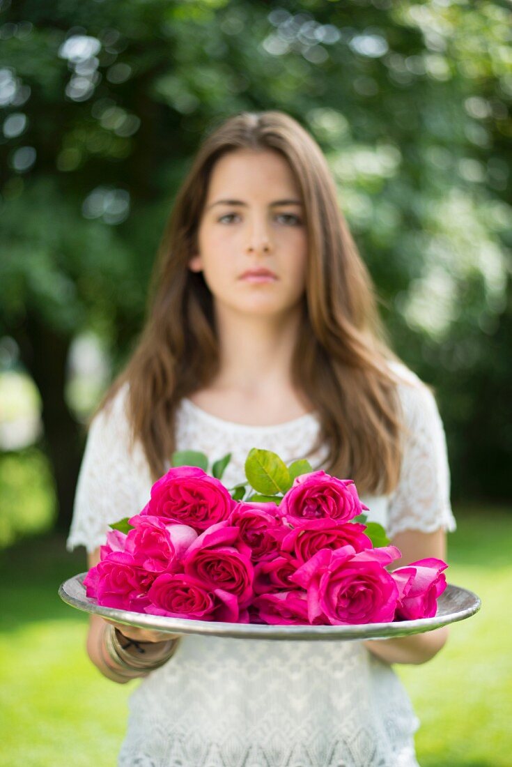 Mädchen hält Tablett mit pinkfarbenen Rosen