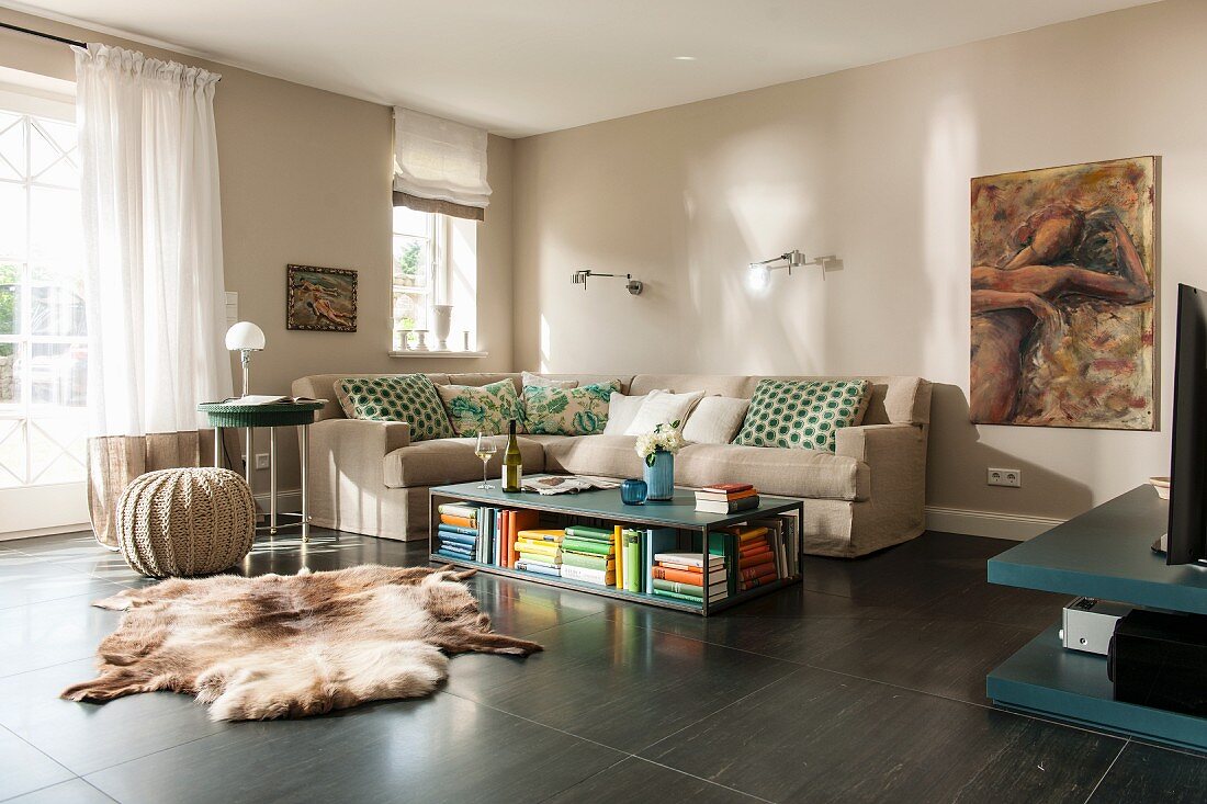 Gemütliche Loungeecke mit beigefarbenen Wänden, Sofa übereck und Bodentisch, davor Tierfell auf dunklem Boden