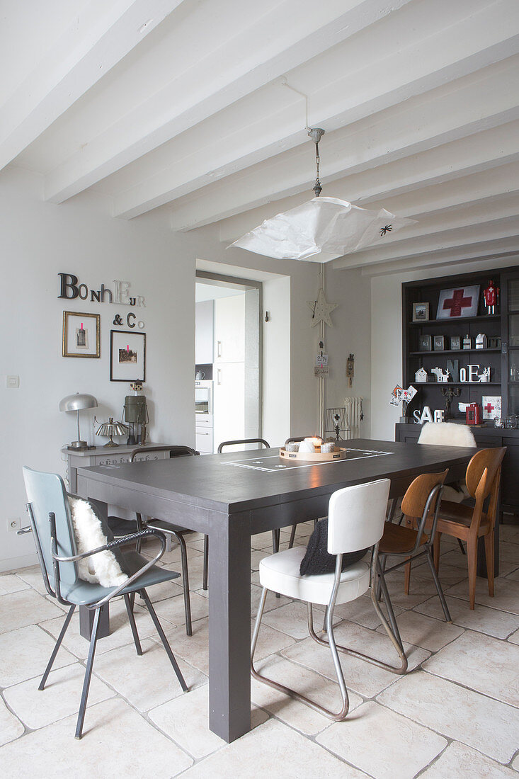 Various retro chairs around grey table in dining room with white wood-beamed ceiling