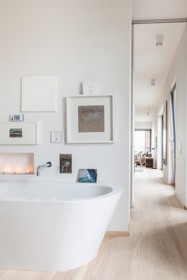 Free-standing bathtub below gallery of pictures and view into living room