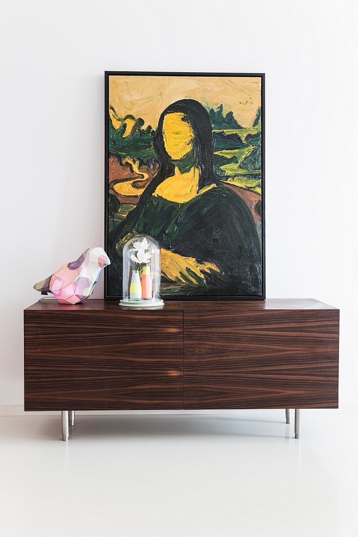 Modified painting of Mona Lisa, bird-shaped table lamp and vases below glass cover on top of sideboard