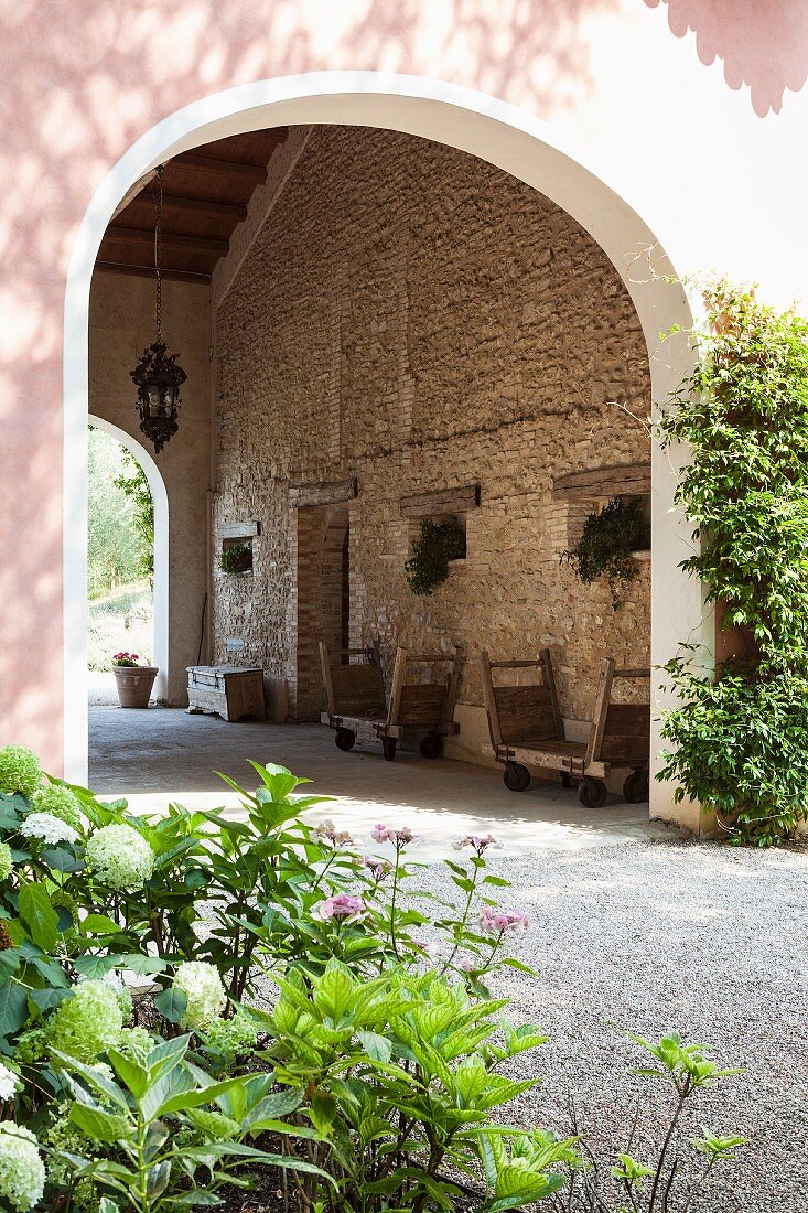 Blick auf Durchfahrt eines mediterranen Landhauses, traditionelle Holzwägen vor Natursteinwand