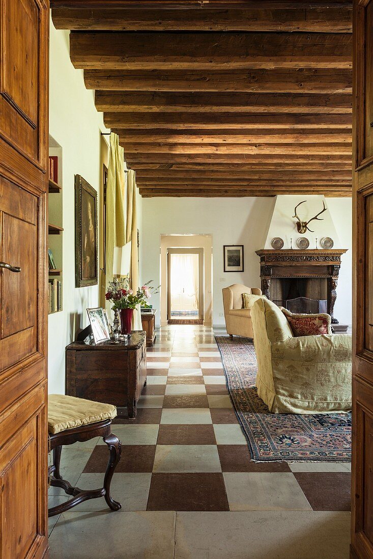 Blick durch offene Tür in Loungebereich mit rustikaler Holzbalkendecke und Schachbrettmusterboden