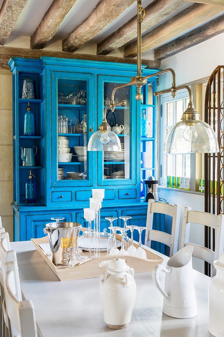 Blick über Esstisch unter Vintage Pendelleuchte auf blau lackierten Vitrinenschrank in rustikalem Esszimmer