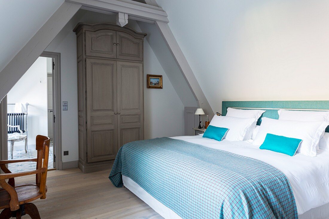 Doppelbett mit blau karierter Tagesdecke und weisser Bettwäsche im Dachgeschoss