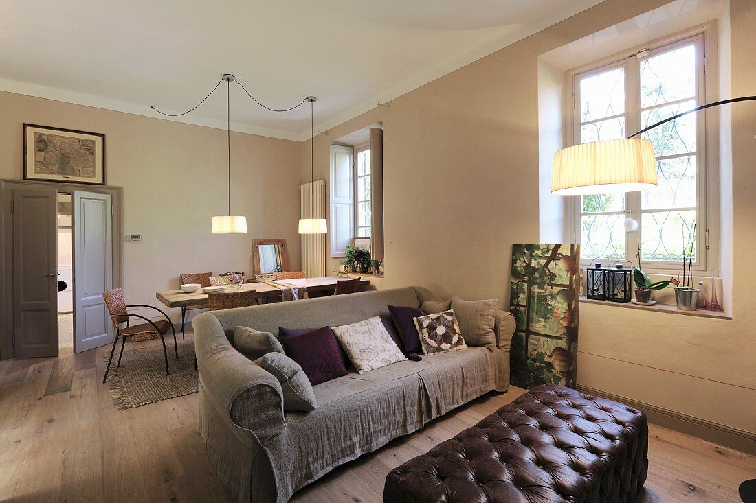 Bogenlampe über Leder-Polstertisch und Sofa mit beigefarbener Husse, im Hintergrund Essplatz in offenem Wohnraum