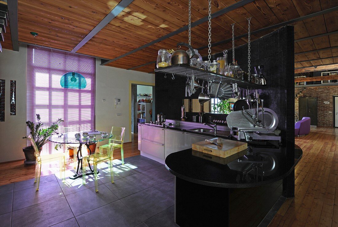 Transparent plastic chairs around dining table and purple blinds in open-plan kitchen of industrial-style loft apartment