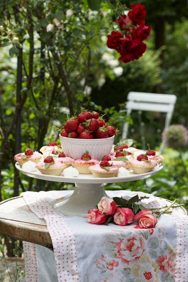 Tortenplatte mit Erdbertörtchen und einer Schale Erdbeeren