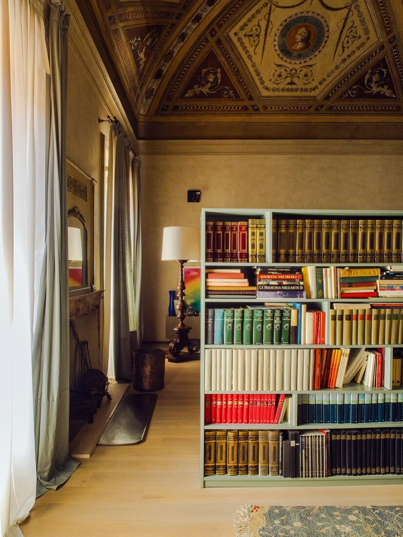 Wohnzimmer in einem Palazzo mit hoher, bemalter Decke, ein Bücherregal als Raumteiler