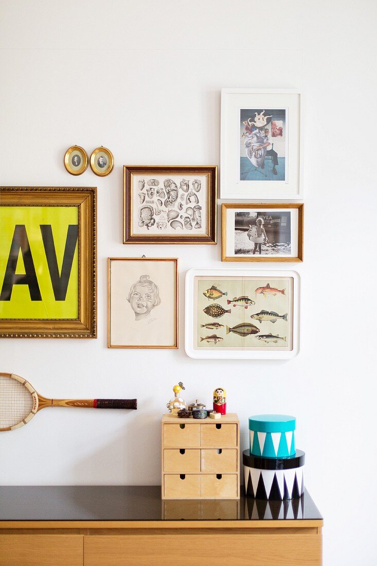 Holzkästchen mit Schubladen und Schachteln auf Sideboard vor Wand mit Bildergalerie und aufgehängtem Tennisschläger