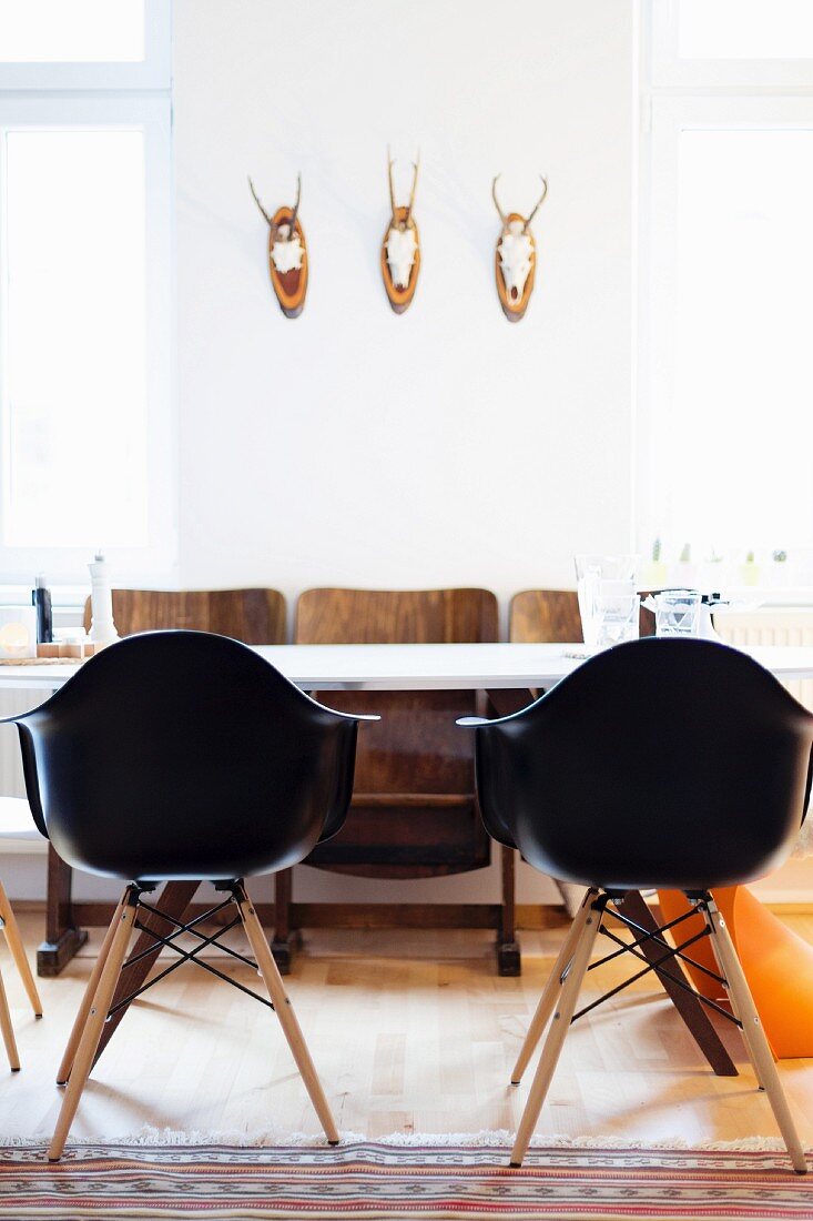 Black shell chairs around white table and retro cinema seats below three hunting trophies on wall