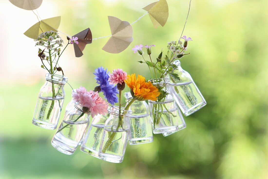 Eine Girlande mit Sommerblumen in Glasfläschchen und eine Papiergirlande für den Garten