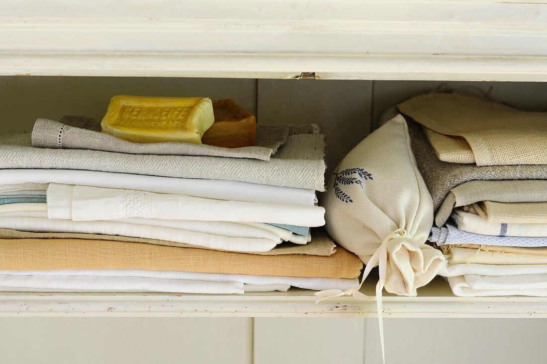 Gestapelte Tischtücher, Seifen und Lavendelsäckchen im Wäscheschrank