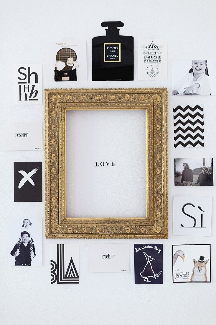 Postkarten und Fotos mit verschiedenen Motiven um goldenen Bilderrahmen mit 'Love'-Botschaft an Wand