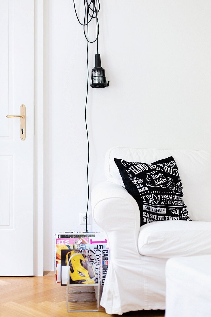 White loose-covered sofa and magazine rack below work lamp hung on wall