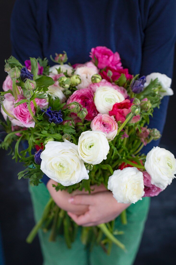 Hands holding bouquet of ranunculus and anemones
