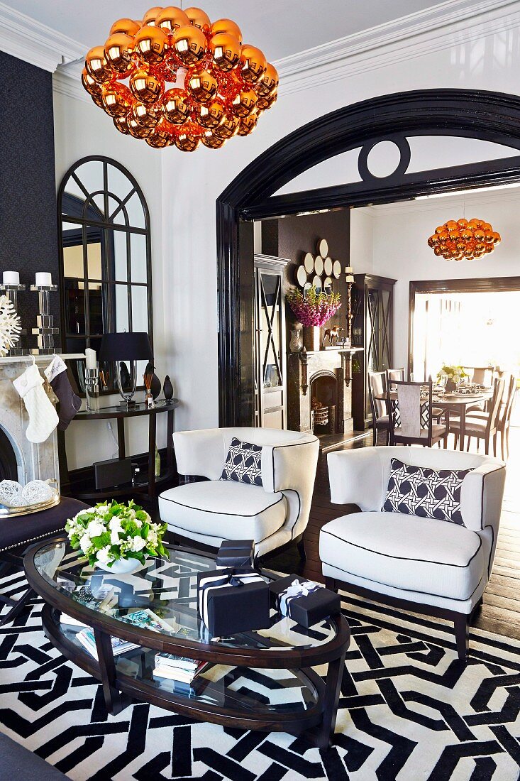 Edler Loungebereich in schwarzweißem Farbkonzept mit Durchgang und orangefarbenen Designer-Pendelleuchten