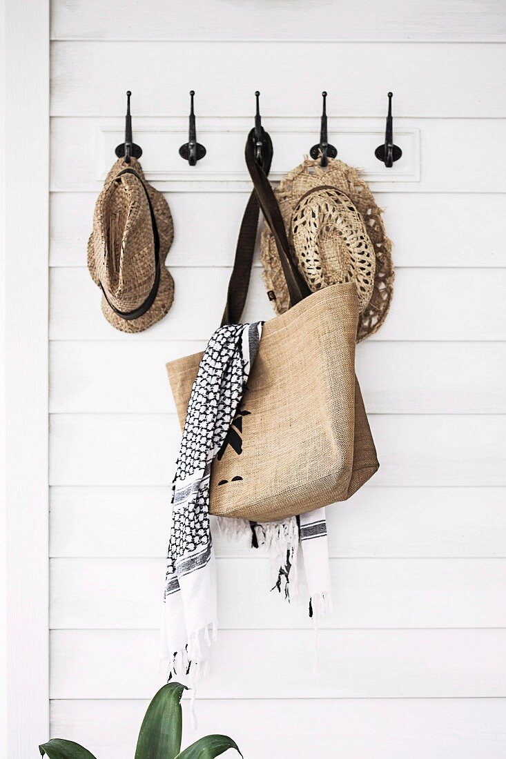 Vintage hook bar with straw hats and shopping bag on white wooden paneling