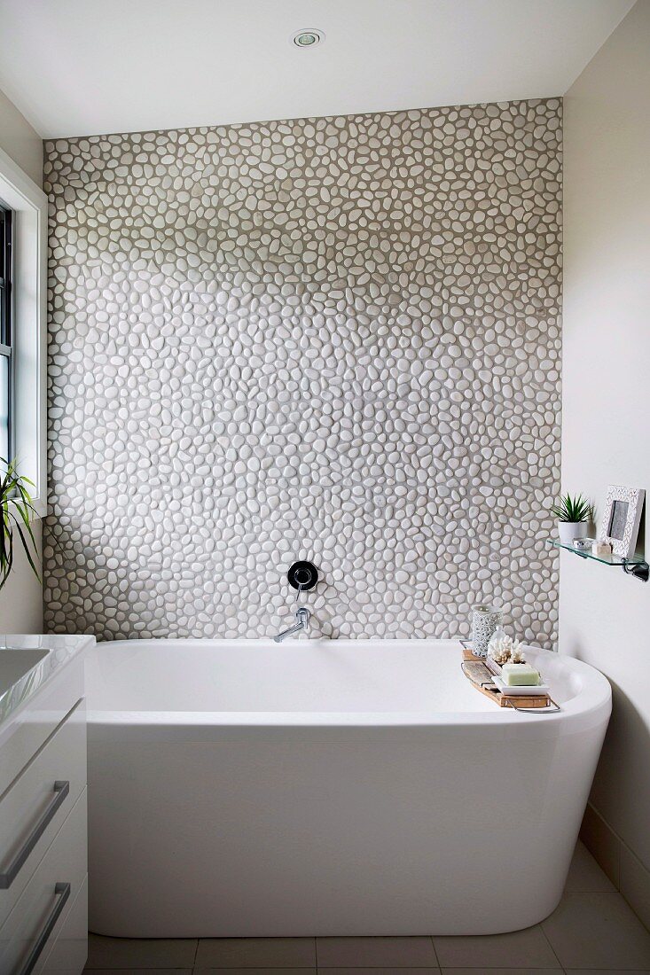 Freestanding bathtub in front of wall with pebble wall