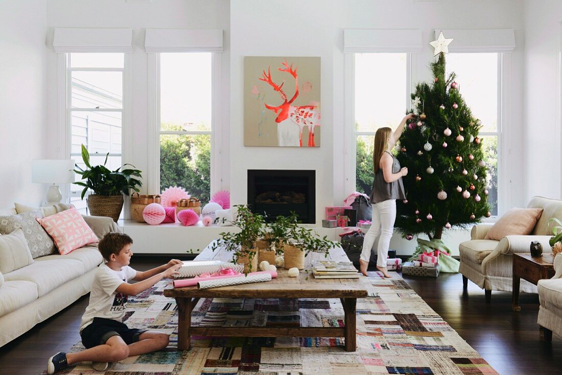 Jugendliche schmückt Weihnachtsbaum und Junge verpackt Weihanchtsgeschenk in zeitgenössischem australischem Wohnambinete