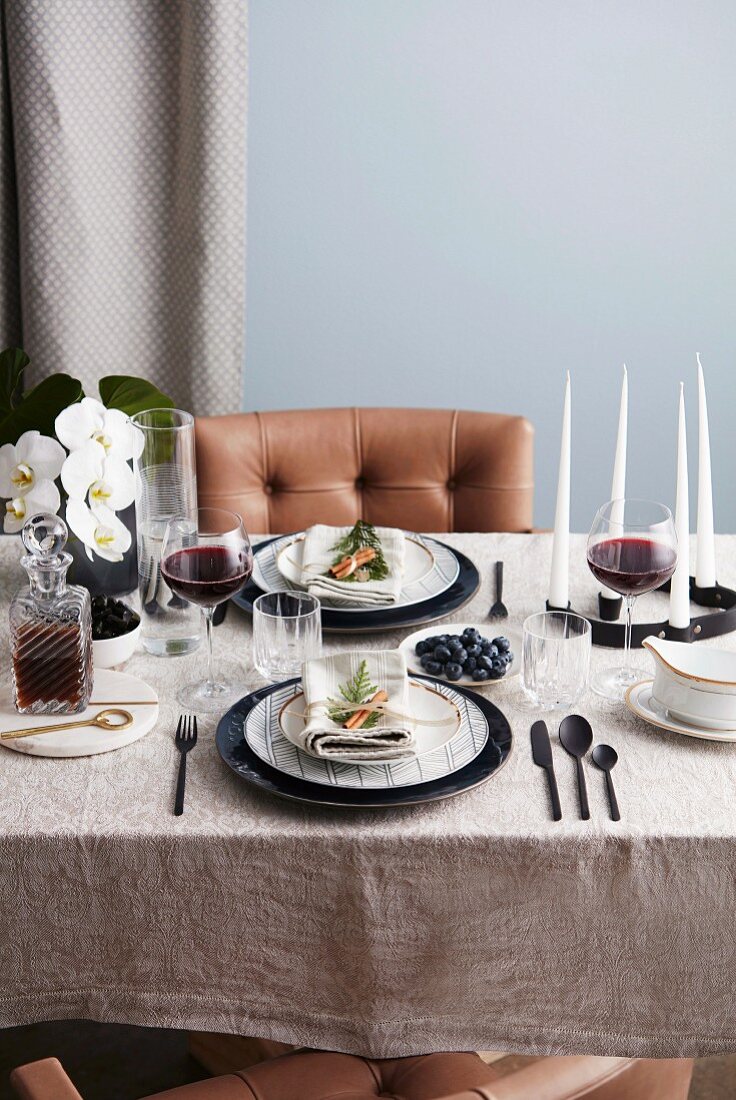 Gedeckter Tisch mit schwarzem Besteck, Rotweingläsern, Kerzen und Orchideen