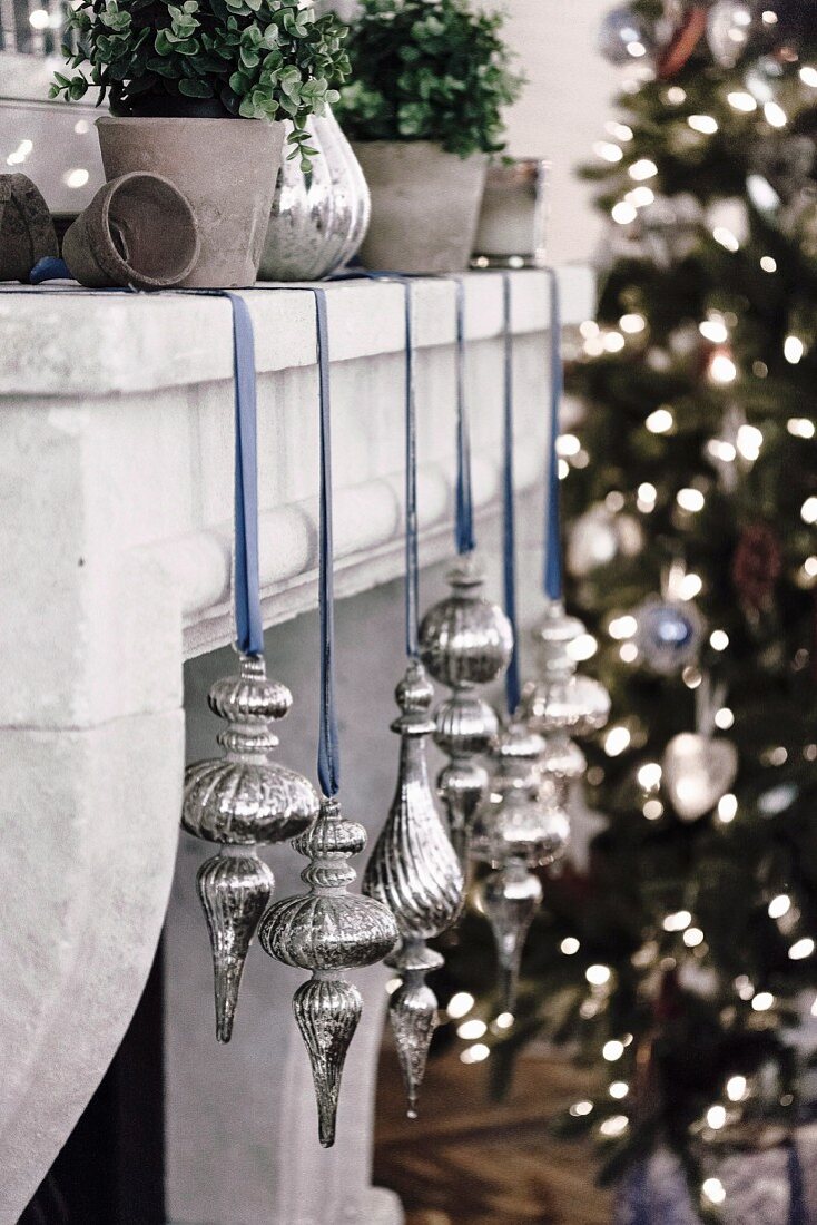 Weihnachtssschmuck in Silber mit blauem Schleifenband an Kaminsims aufgehängt