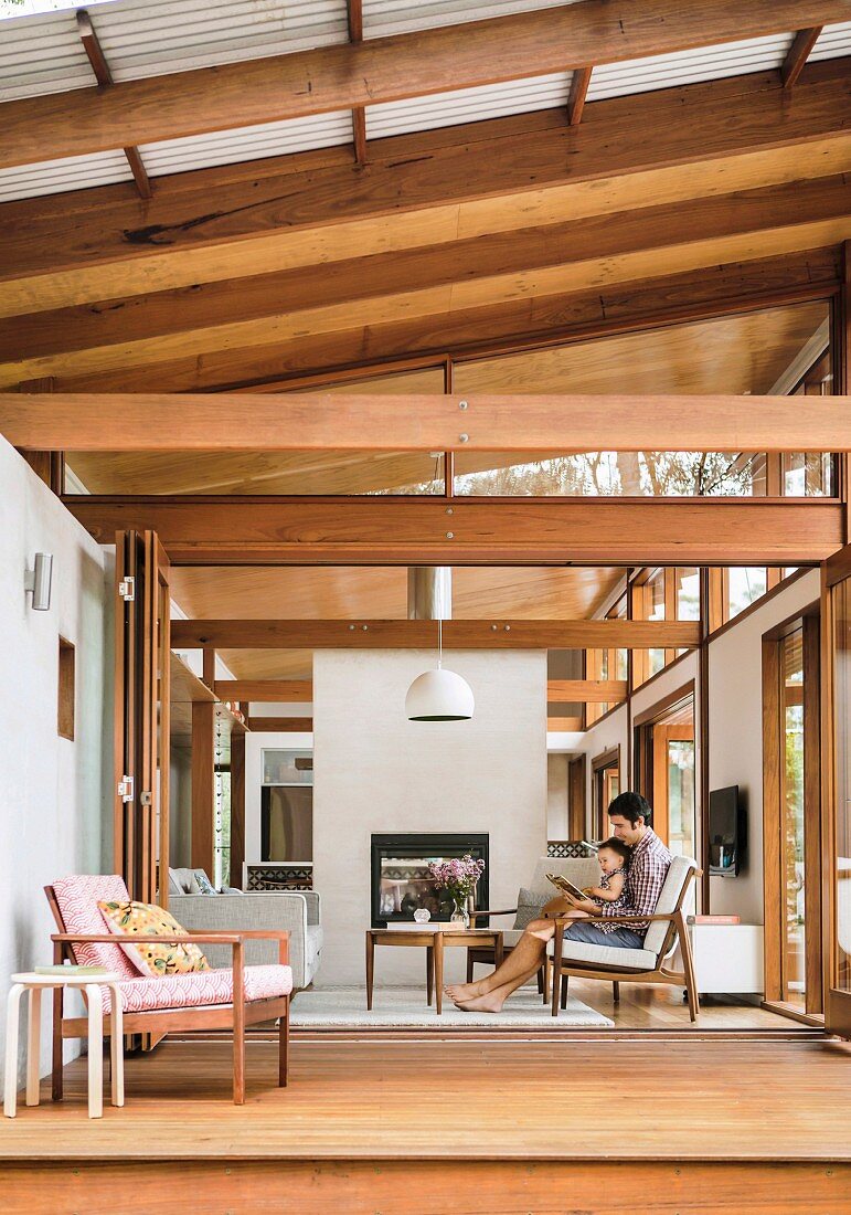 Blick auf Holzterrasse und Wohnraum mit Holzkonstruktion und schlichtem asiatischem Flair, Vater und Kind auf gemütlichem Sessel