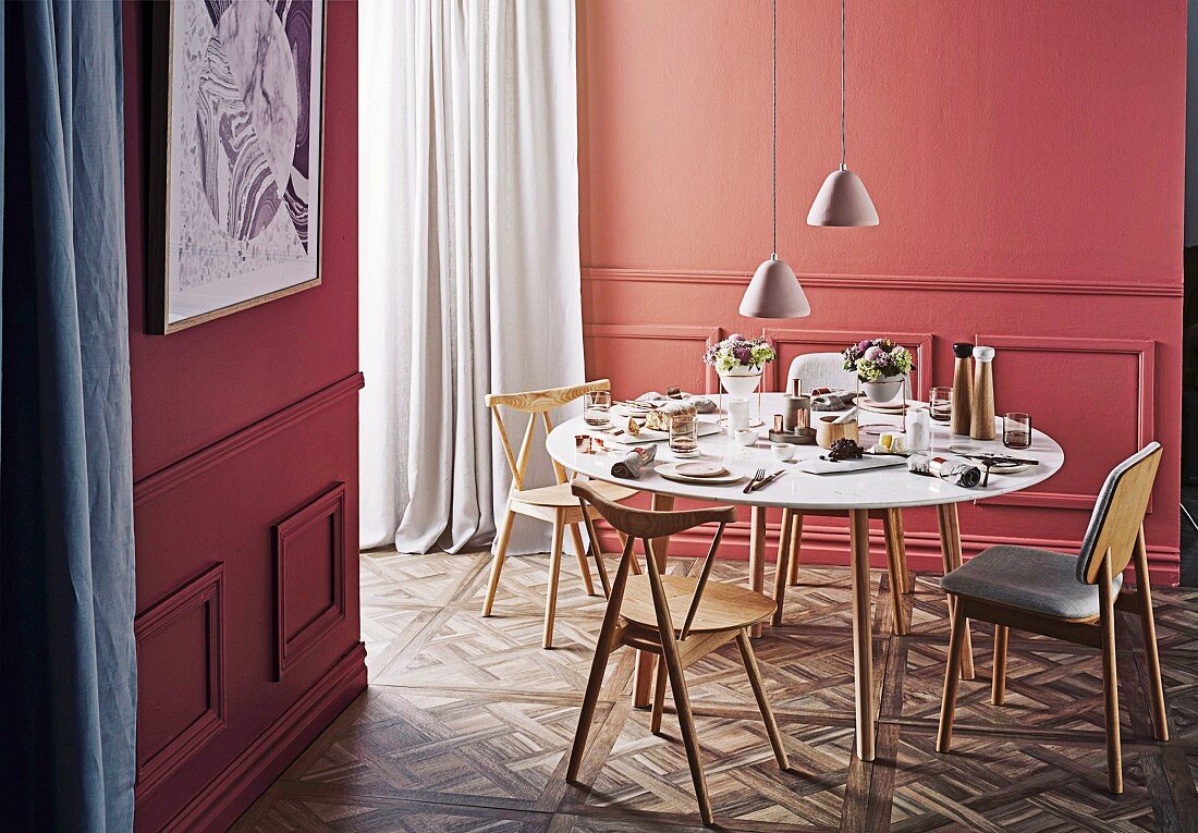 Runder gedeckter Tisch mit Holzstühlen vor lachsfarbener Wand