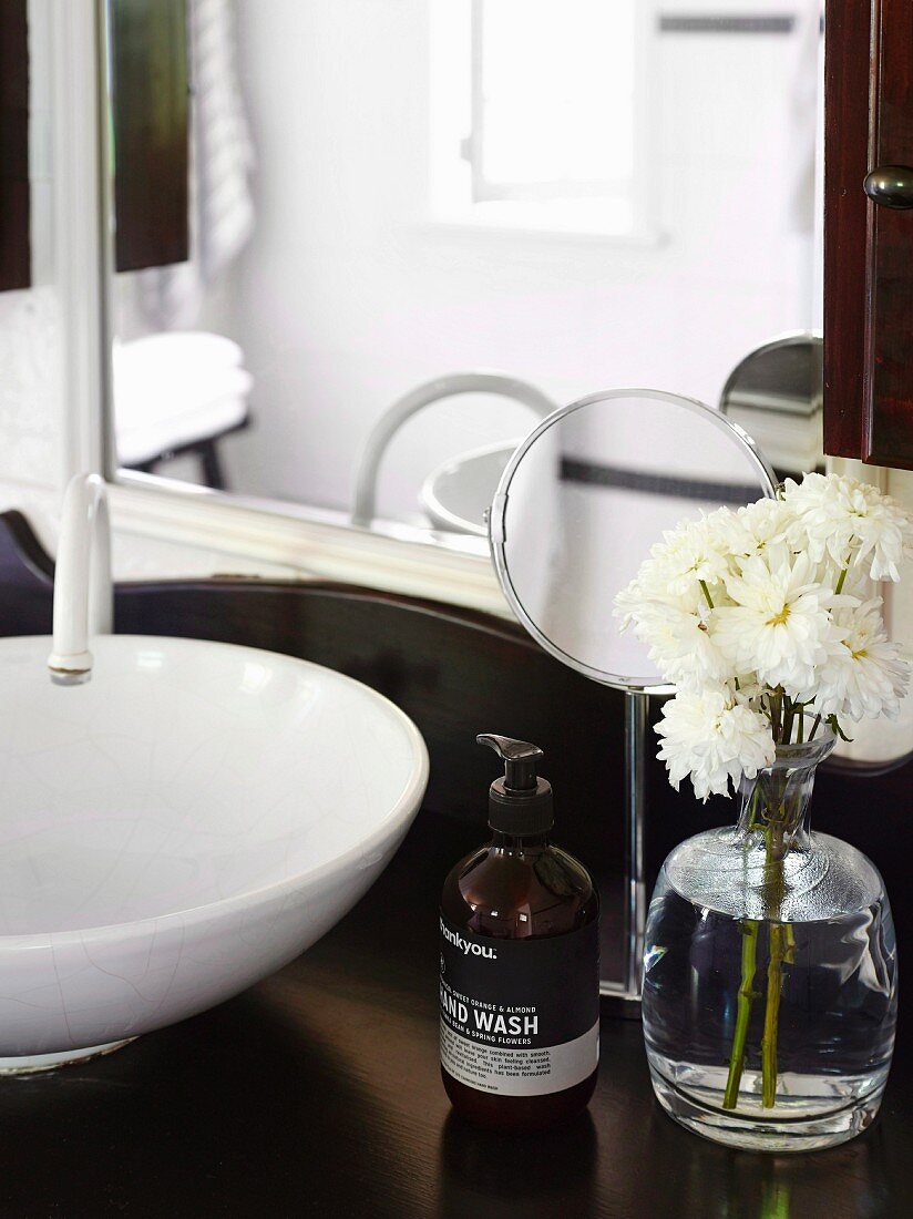 weiße Blumen und Seifenspender vor Kosmetikspiegel auf Waschtisch mit traditionellem Flair