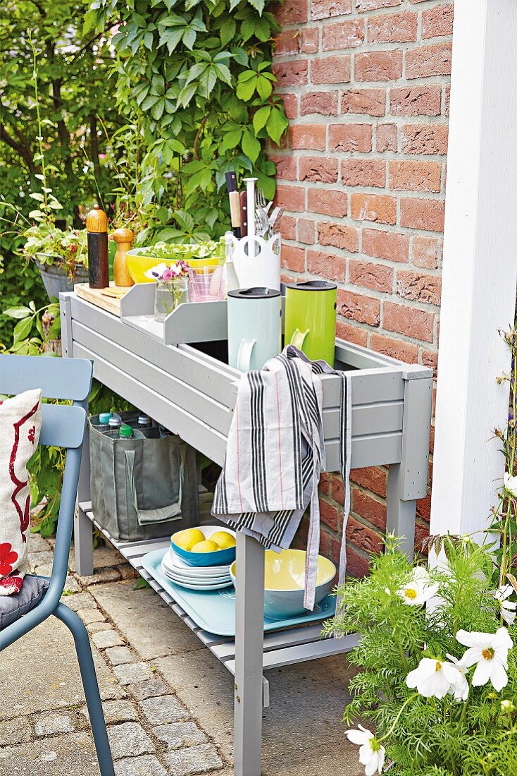 A grey painted potting table as a serving table with Thermos flask, cooking utensils and crockery on a table