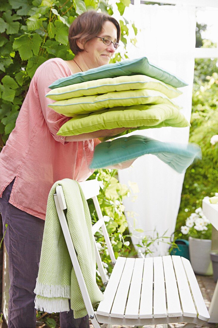A woman at a garden bench holding cushions