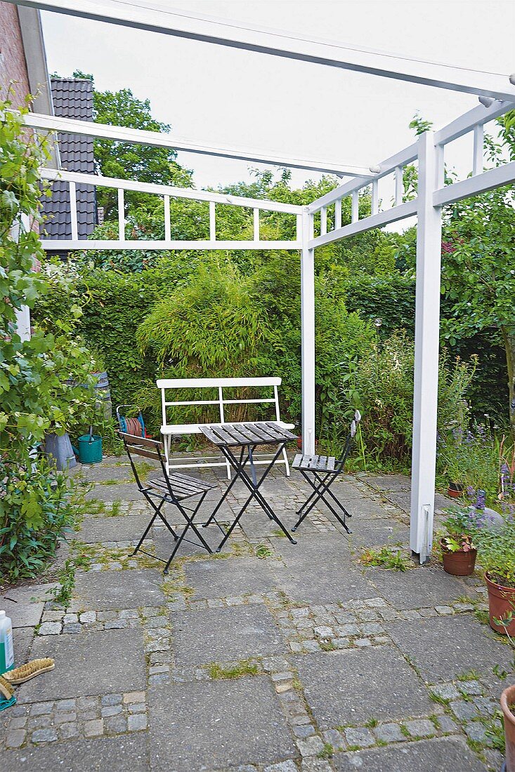 Gartenstühle und Tisch auf Terrasse mit weiss lackiertem Pergolagestell und Betonplatten