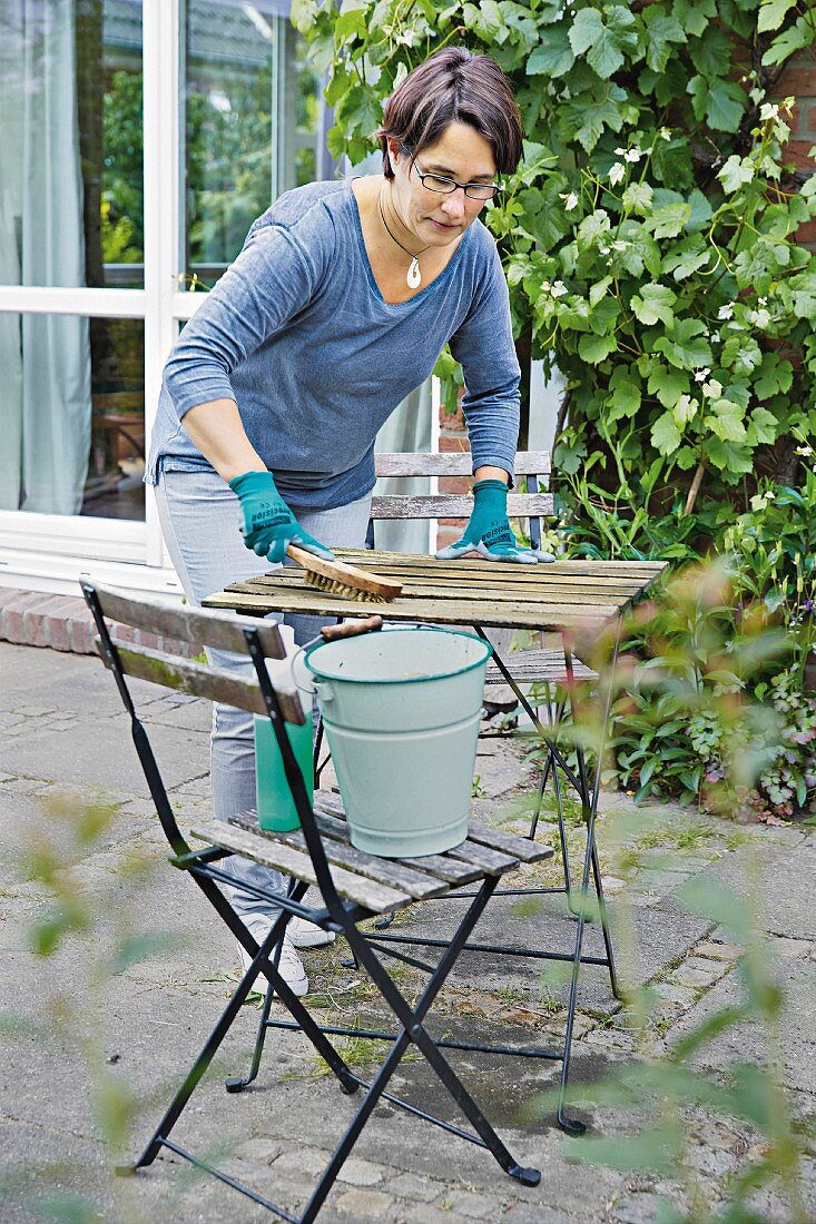 Frühjahrsputz auf der Terrasse, Frau beim Putzen des Gartentisches