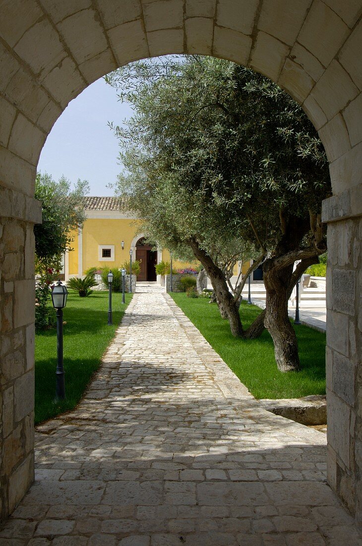View through Mediterranean archway along paved path leading through garden