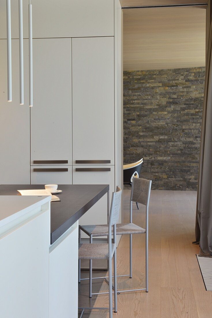 Minimalist dining area in front of partition cabinets next to doorway with view of stone wall