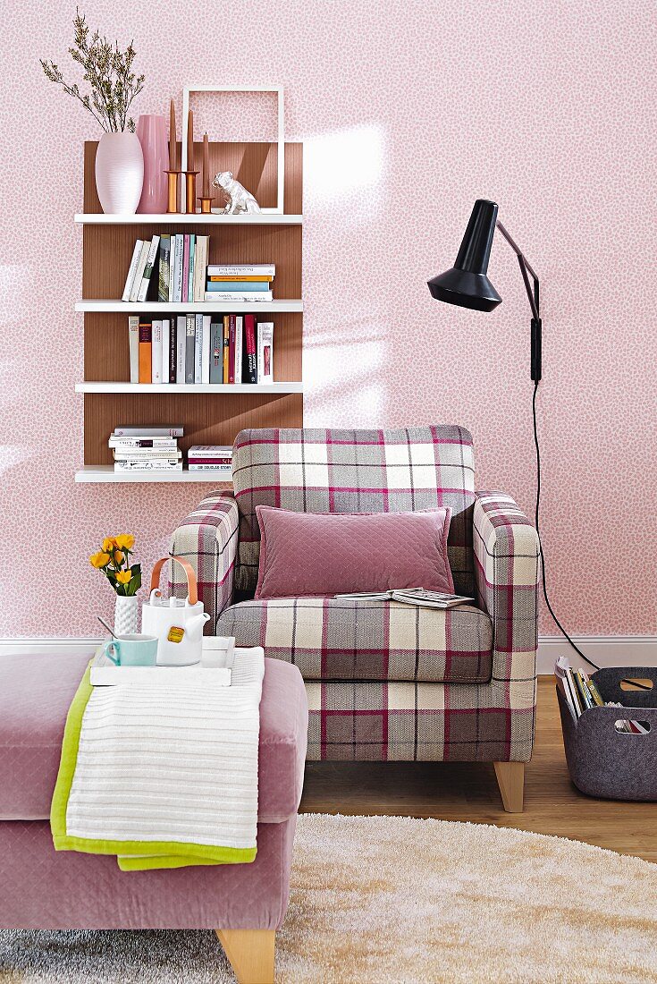 A checked upholstered armchair with a footstool against a purple wall with a wall shelf
