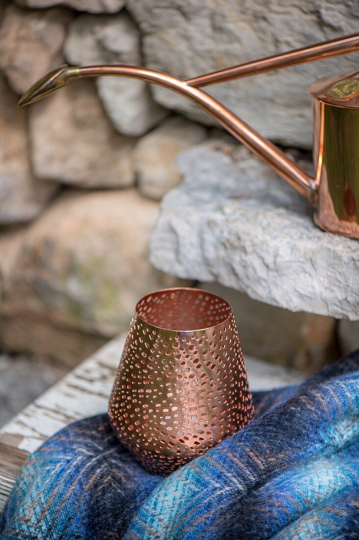 Perforated copper tealight holder in front of stone wall
